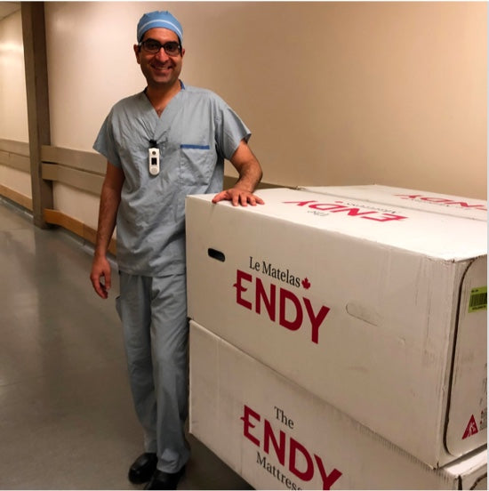 One BC Women's Hospital healthcare worker wearing scrubs and posing with a boxes of the Endy Mattress.